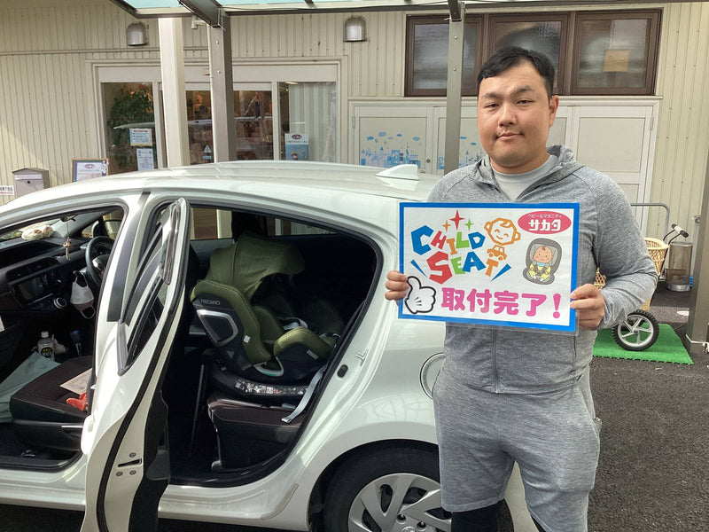 白い車に取り付けたグリーンのチャイルドシートと、お客様